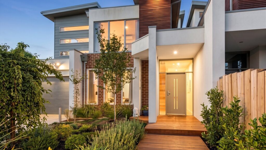 Dusk view of a townhouse entry in Chelsea with a timber deck and glowing interior lighting