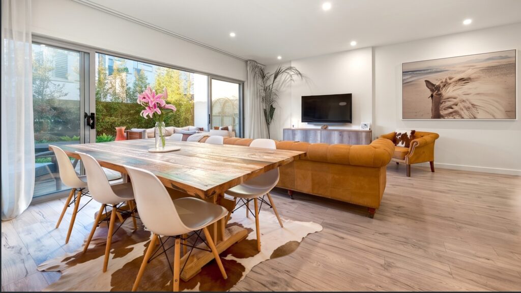 Open plan living and dining area with a wood dining table, tan leather sofa and sliding doors to the rear garden